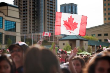 Canadian flag waved over a crowd in a busy urban setting 