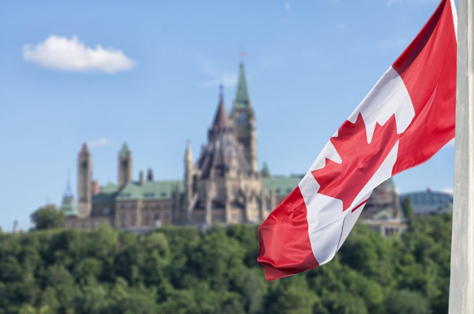 A Canadian flag fluttering with a view of Ottawa's parliment hill in the background.