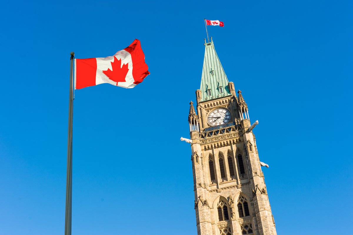 Canada flag 
 against the blue sky with parliament in the background/