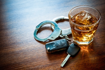 A set of car keys, hancuffs, and a glass of liquor on a table